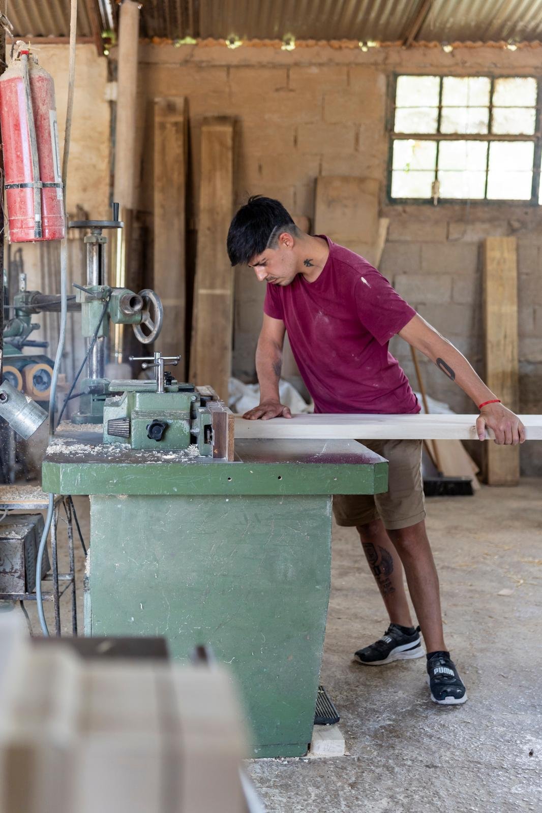 carpintero ensamblando el armazón de una silla de madera maciza en taller, con prensas y herramientas sobre banco de trabajo, plano general con luz artificial cálida