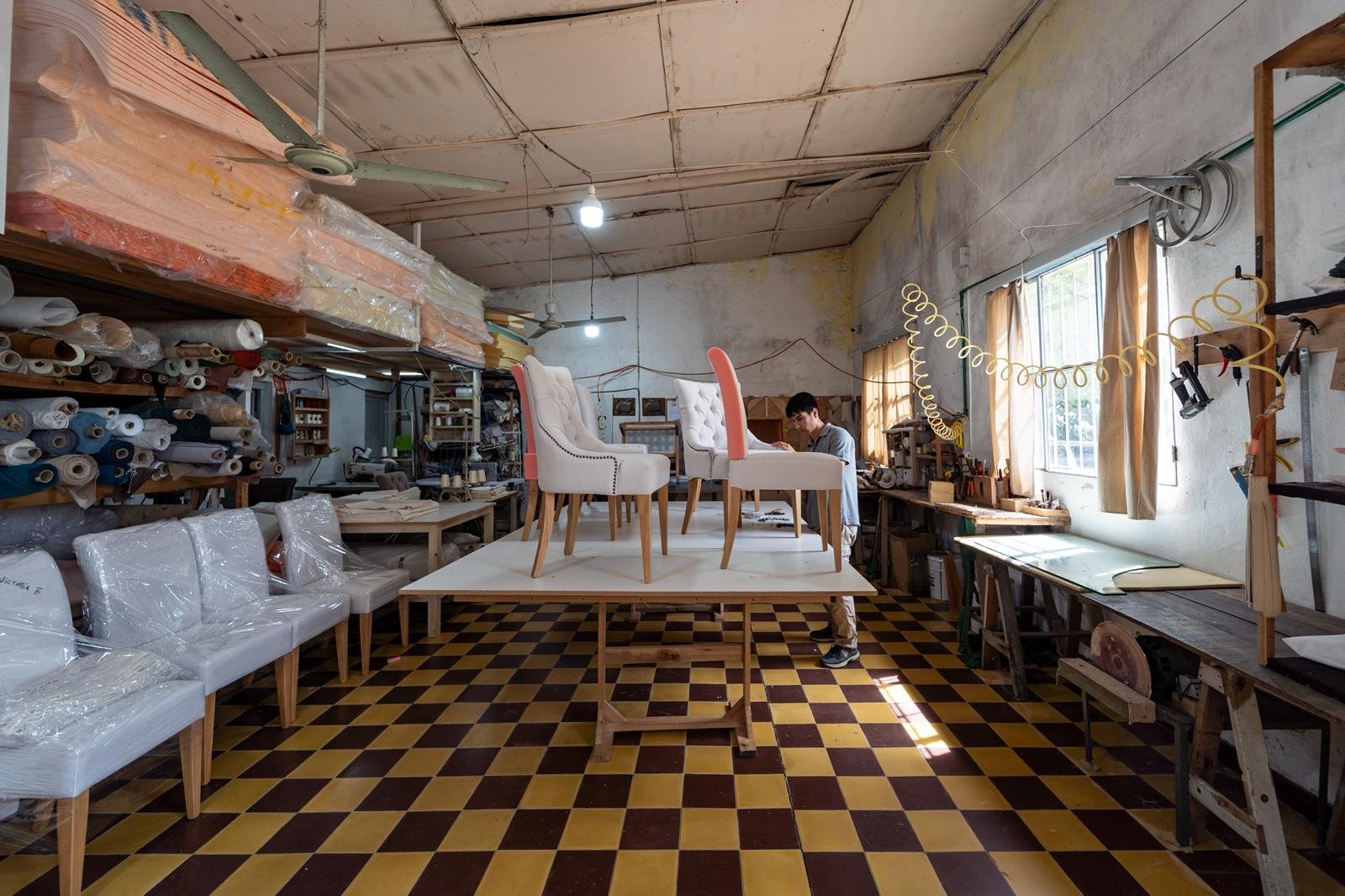 plano general del taller de tapicería de Marvic con sillas en proceso de tapizado en tela Aqua Clean, herramientas y mesas de trabajo visibles, luz cenital