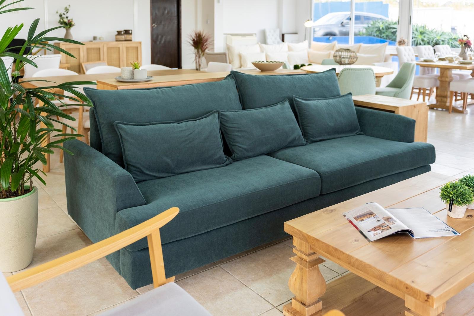 interior del showroom con sofá tapizado en tela aqua clean y mesa de fresno macizo al fondo, luz natural lateral, plano general