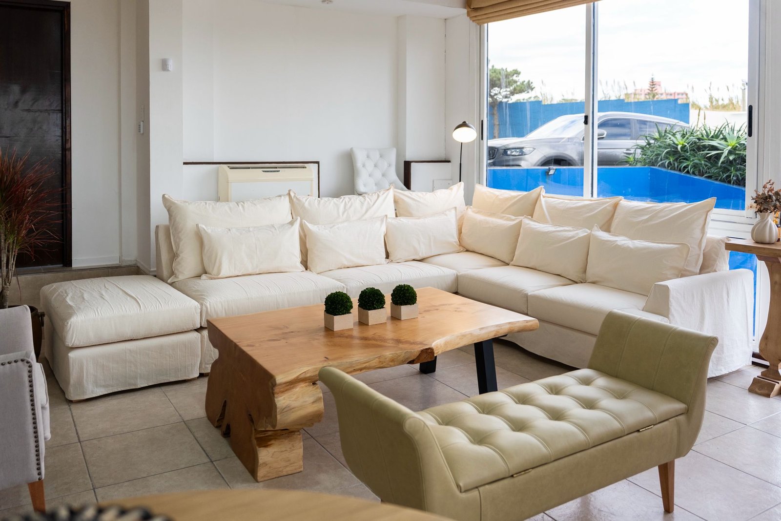 plano general de una sala de estar luminosa con una mesa ratona de madera maciza natural al centro, sillones en tono gris claro, luz de tarde entrando por una ventana lateral